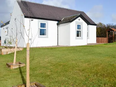 a small white house with a tree in a yard at Broomlands Cottage in Beattock