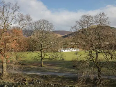 a field with trees and a house in the distance at Oak View in Keswick