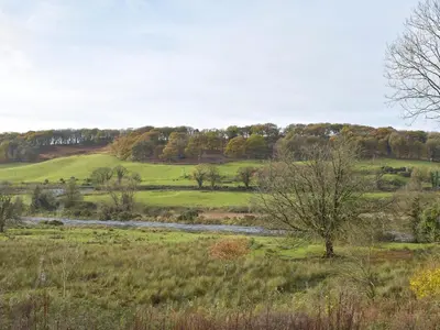 a grassy field with a river in the middle at West Lodge - Uk7137 in Newton Stewart