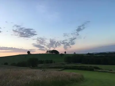 a field of grass with a sunset in the sky at Shepherds Hut-hot tub hire-dog friendly-views in Dumfries