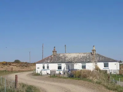 a white house on the side of a dirt road at Kirklauchline Cottage in Portpatrick