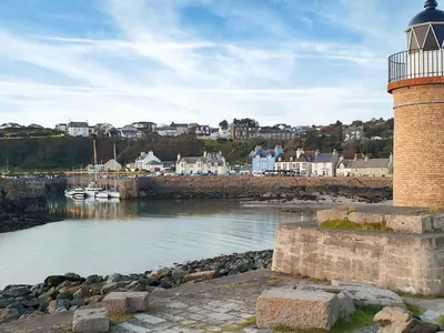 a lighthouse next to a body of water with boats at Kirklauchline Cottage in Portpatrick