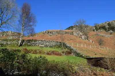a grassy hill with a stone wall and a fence at End Cottage, Chapel Stile in Chapel Stile