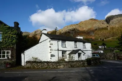 a white house with mountains in the background at Stickle Cottage, Great Langdale in Grasmere