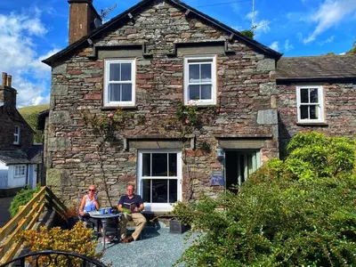 two people sitting in front of a stone house at Juniper Grasmere - Juniper Cottage, Grasmere in Grasmere