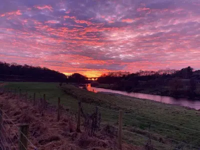 a sunset over a field with a fence and a river at Cottage at Inch Farm solitude beside the River in Longtown
