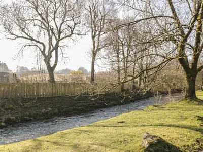 a river with a fence and some trees and grass at Beckside Cottage in Welton