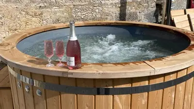a hot tub with a bottle of wine and two wine glasses at 2-Bed Barn Hot Tub & Pet Friendly near Muirkirk in Cumnock