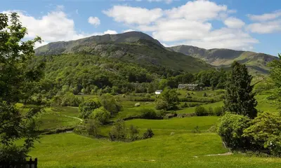 a green field with a mountain in the background at Oxen Fell Cottage in Little Langdale