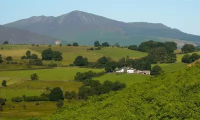 a house on a green hill with mountains in the background at Nest Barn in Keswick