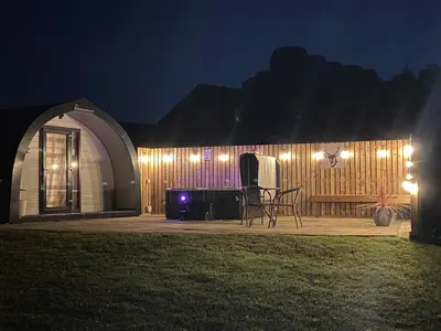a building with lights on the side of it at night at The Stag Pod Farm Stay with Hot Tub Sleeps 2 in Galston