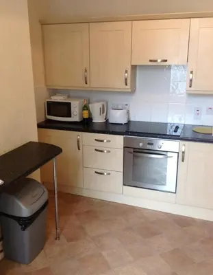 a kitchen with white cabinets and a microwave and a table at Arrandale Apartments in Douglas