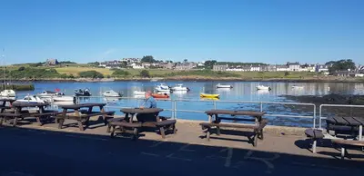 a group of picnic tables and boats in the water at The Steam Packet Inn in Isle of Whithorn