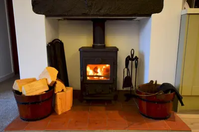 a fireplace with two barrels of wood and a stove at Bottom Shop, Elterwater in Chapel Stile