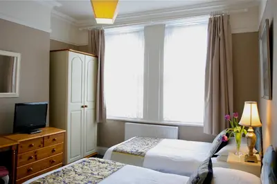 a bedroom with two beds and a tv and windows at Melrose Guest House in Douglas