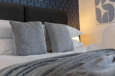 a bed with blue and white pillows on it at Main Street View - Donnini Apartments in Prestwick