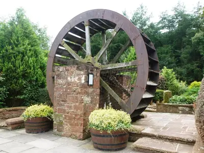a wooden waterwheel in a garden with two potted plants at The Mill Forge Hotel in Gretna Green