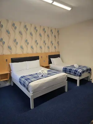two beds in a room with blue carpet at The Mill Forge Hotel in Gretna Green