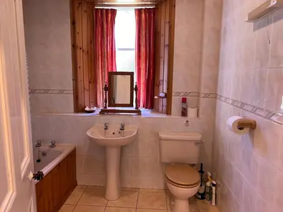 a bathroom with a sink and a toilet and a window at Laundry Cottage in Lanark