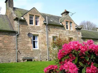 a stone house with pink flowers in front of it at Laundry Cottage in Lanark