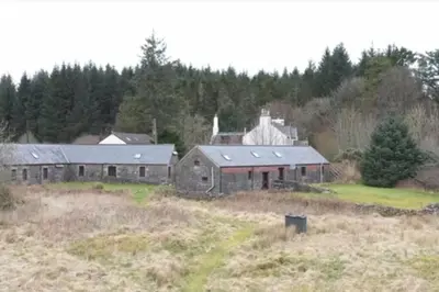 an old barn in a field next to a forest at Merrick Cottage in Bargrennan