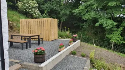 a patio with a table and a bench and flowers at Dairy Cottage with sea views in Girvan