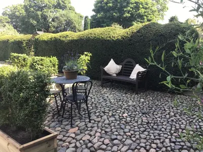 a garden with a table and chairs and a hedge at Historic converted byre in courtyard of 16C house in Caldbeck