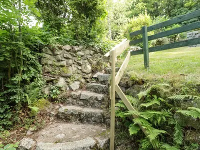 a wooden stairway with a bench next to a stone wall at Wood End in Dalbeattie