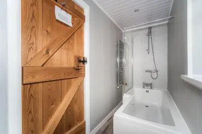 a bathroom with a wooden door and a bath tub at Acorn Cottage in Keswick
