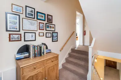 a hallway with a staircase with a wooden dresser and framed pictures at The Ridgeway in Keswick