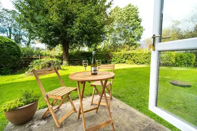 a table with two chairs and wine glasses on a patio at Quaver Cottage in Keswick