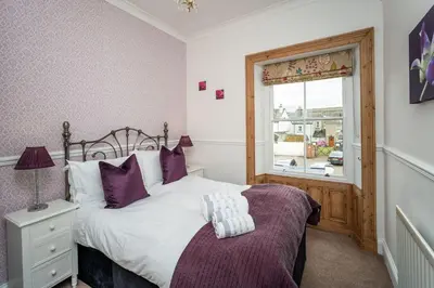 a bedroom with a bed with purple pillows and a window at Bridge Cottage in Keswick