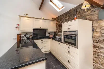 a kitchen with white cabinets and a stone wall at Bridge Mews in Keswick