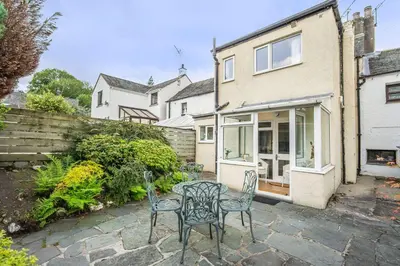 a patio with two chairs and a table in front of a house at Millside Cottage in Braithwaite