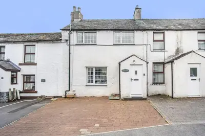 a white house with a white door on a street at Millside Cottage in Braithwaite