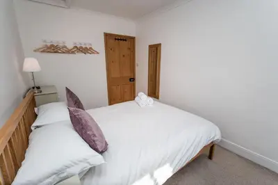 a bedroom with a bed with white sheets and purple pillows at Coleridge Cottage in Keswick