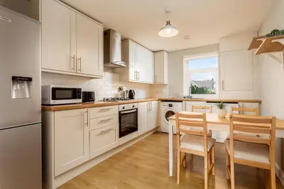 a kitchen with white cabinets and a table and chairs at Shore View - Donnini Apartments in Prestwick