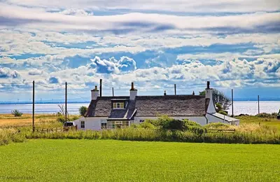 a house sitting in a field next to the ocean at Arthur's Cottage in Dumfries