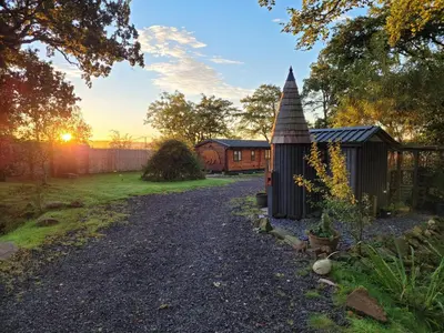 a garden with a small house and a gravel driveway at Cosy wood cabin in rural area near national park in Cumnock