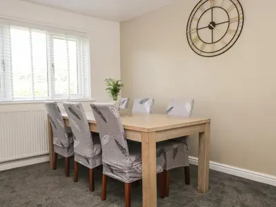 a dining room table with chairs and a clock on the wall at 26 Hycemoor Way in Millom