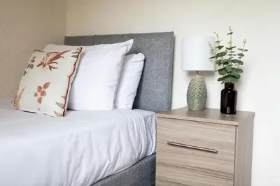 a bed with white sheets and a lamp on a night stand at Adrian House, near Hospital, easy parking + garden in Carlisle
