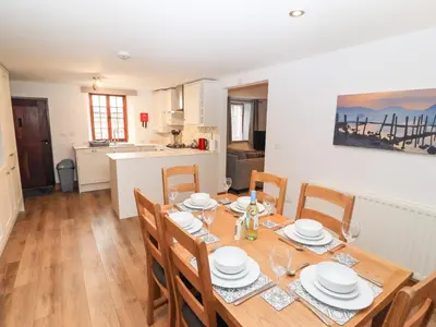 a dining room with a table and chairs and a kitchen at Fryston Cottage in Keswick