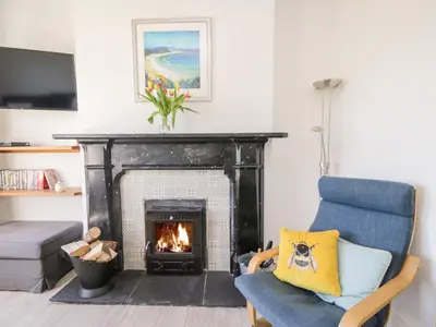 a living room with a fireplace and a blue chair at Pow-Wow Shore Cottage in Annan