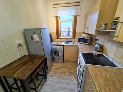 a small kitchen with a table and a refrigerator at Lovely self-catering apartment in city centre in Dumfries