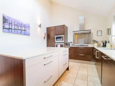 a large kitchen with white counters and wooden cabinets at Cloud End in Keswick