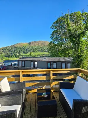 a deck with chairs and tables and a house at Unique Caravan with Outdoor Space Lodge in Ballantrae
