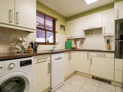 a kitchen with white cabinets and a washer and dryer at Derwent Haven in Keswick