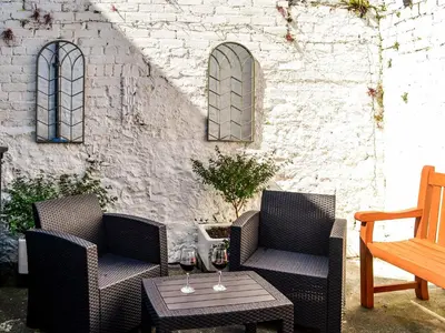 a patio with two chairs and a table with wine glasses at Hammy's Cottage in Drummore