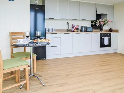 a kitchen with white cabinets and a table with wine glasses at The Seaview Snug in Whithorn