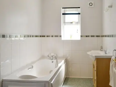 a white bathroom with a tub and a sink at Curlew Cottage in Dinwoodie Mains